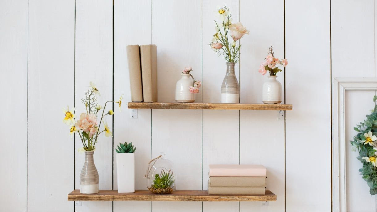 photo of two offset natural wood shelves on a white wood paneled wall, styled with books and plants